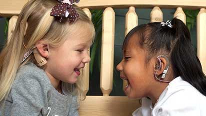 Two girls with cochlear implants smiling at each other