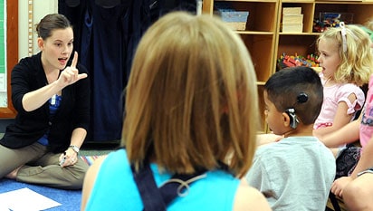 Girl with cochlear implant and boy with hearing aid reading and smiling